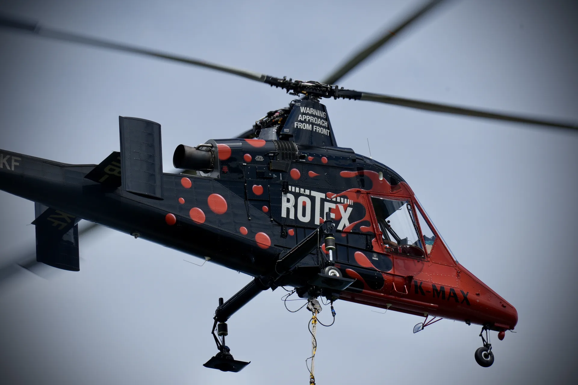 Kaman K-MAX Helikopter im Flug vor bewaldeten Hügeln