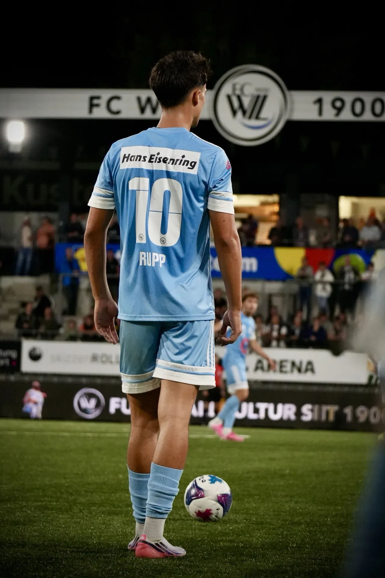Spieler mit Ball an der Eckfahne vor der Tribüne